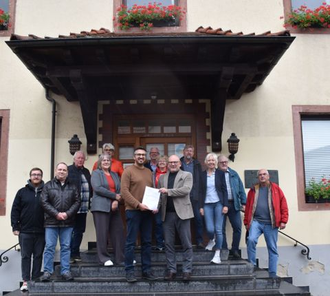 Bürgermeister Matthias Horlacher (vorne links) nahm in im Beisein von Mitgliedern der Steuerungsgruppe und des Gemeindevorstands von Landrat Frank Matiaske (vorne rechts) entgegen.